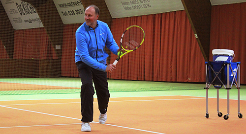 Momentaufnahme des Tennis Trainers Dimitri, der mit seinem Tennisschläger ausholt, um den Tennisball in einer Halle zu treffen.